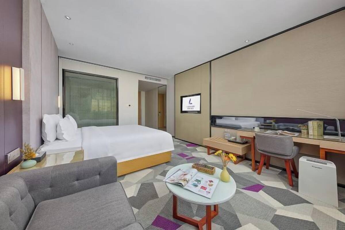 Quarto de hotel moderno com uma cama grande, uma escrivaninha, uma cadeira, uma mesinha e uma televisão.