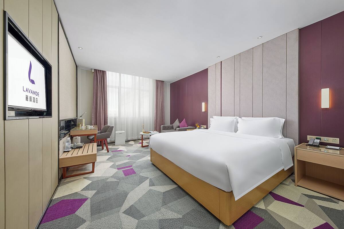 Quarto de hotel com uma cama grande, uma escrivaninha, uma cadeira, uma mesinha e uma televisão.