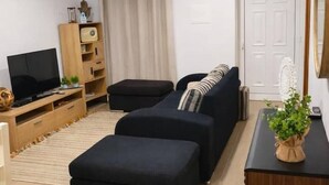 Sala de estar com sofá, banquinho, televisão, armário de madeira e planta em vaso.