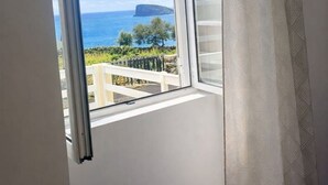 Quarto com uma grande janela que oferece vista para o mar e uma ilha distante.