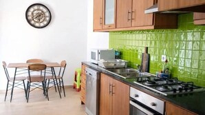 Uma cozinha moderna com armários de madeira, painel de fundo verde, área de refeições com cadeiras e um relógio na parede.