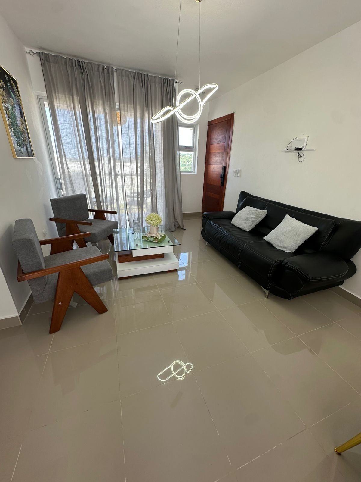 Una sala de estar moderna con un sofá de cuero negro, sillones grises y una mesa de centro de vidrio.