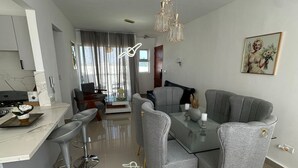 A modern living room with a dining area, grey furniture, and a chandelier. - Apartment near the best beaches (Sosúa)
