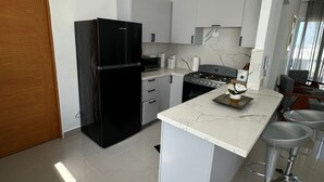 A modern kitchen with a black refrigerator, white cabinets, a marble countertop, and a small island with bar stools. - Apartment near the best beaches (Sosúa)