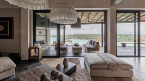 A modern living room with a large sofa, a coffee table, and a dining area. There is a view of a beach and ocean through large windows. - Villa Odeon (Ceningan Island)