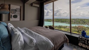 A bedroom with a large window, a bed, a wall-mounted air conditioner, and a framed abstract artwork. - Villa Odeon (Ceningan Island)