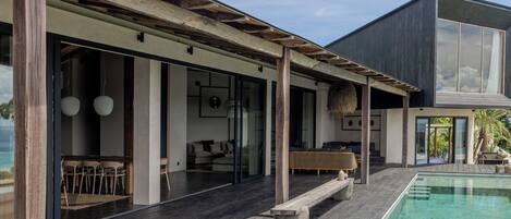 A modern house with a pool, wooden deck, and a dining area with outdoor furniture.