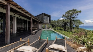 A modern house with a pool, wooden deck, and a view of the ocean. - Villa Odeon (Ceningan Island)