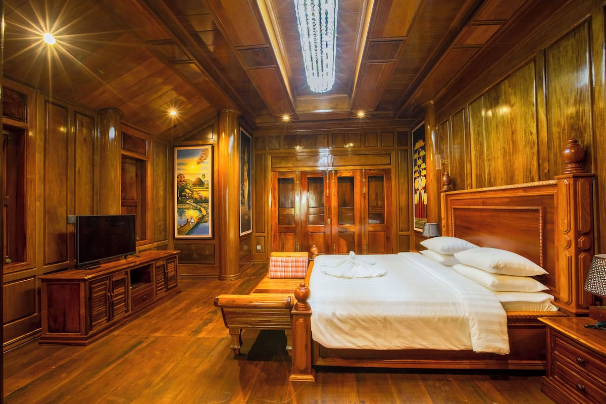 Una habitación con paneles de madera, una cama grande, un televisor y un cuadro en la pared.
