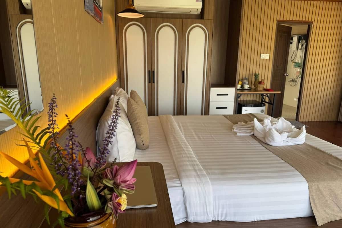 Habitación de hotel con cama, mesita de noche con una computadora portátil, un florero con flores y un baño visible a través de una puerta abierta.