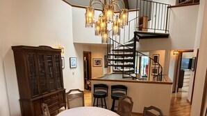 Un comedor amplio con una gran mesa ovalada, sillas de madera, un candelabro y una escalera que sube a un nivel superior.