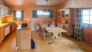 A cozy log cabin with a wooden dining table, chairs, a laptop, and a kitchen area with a stove and cabinets. - Nice home in Rendalen with house a panoramic view (Rendalen)