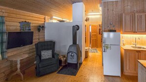 A cozy cabin interior with a wooden interior, a black armchair with a cushion, a wood stove, a white refrigerator, and wooden cabinets. - Nice home in Rendalen with house a panoramic view (Rendalen)
