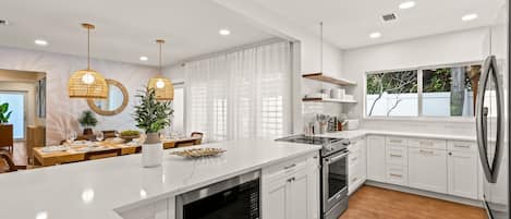 A modern kitchen with white cabinetry, a large island, stainless steel appliances, and pendant lighting.