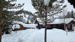 A wooden cabin with a snow-covered roof, surrounded by a wooden fence and snowbanks. - Gorgeous home in Flatdal with sauna (Flatdal)