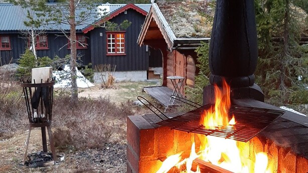 A rustic cabin with a wood-burning stove, a metal chair, and a small table outside. - Gorgeous home in Flatdal with sauna (Flatdal)