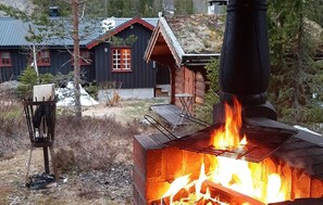 En enkel stuga med en vedeldad kamin, en metallstol och ett litet bord utomhus.