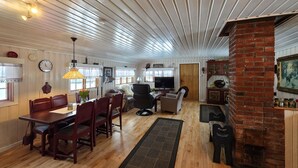 A cozy living room with a dining area, wooden floors, a brick fireplace, and a TV. - Gorgeous home in Flatdal with sauna (Flatdal)