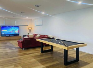 A modern living room with a pool table, a red sofa, a flat-screen TV, and a lamp.