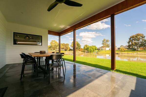 A modern patio with a dining table and chairs, large windows, and a view of a lake.