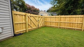 Patio trasero cercado con césped y puerta de madera.