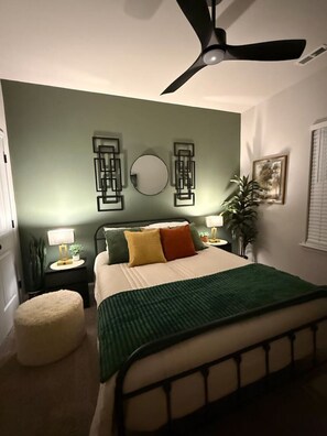 A bedroom with a bed, a ceiling fan, a nightstand with a lamp, and a wall-mounted mirror. - Stylish | Pvt Baths | Minutes to Shopping & Dining (Anderson)