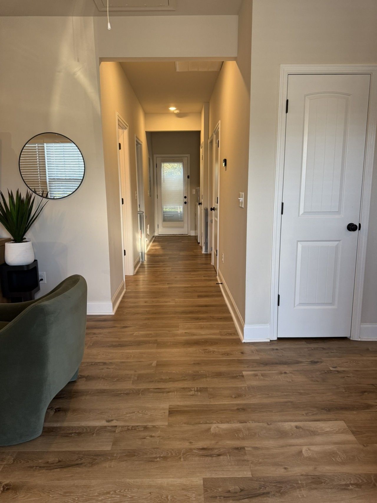 A hallway with wooden flooring, white walls, and a door at the end.