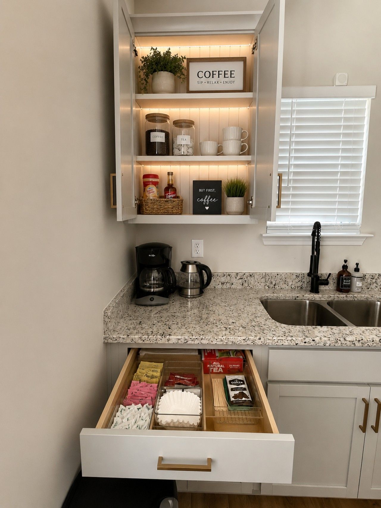 A kitchen with a coffee station, including a coffee maker, cups, and jars labeled coffee and tea.
