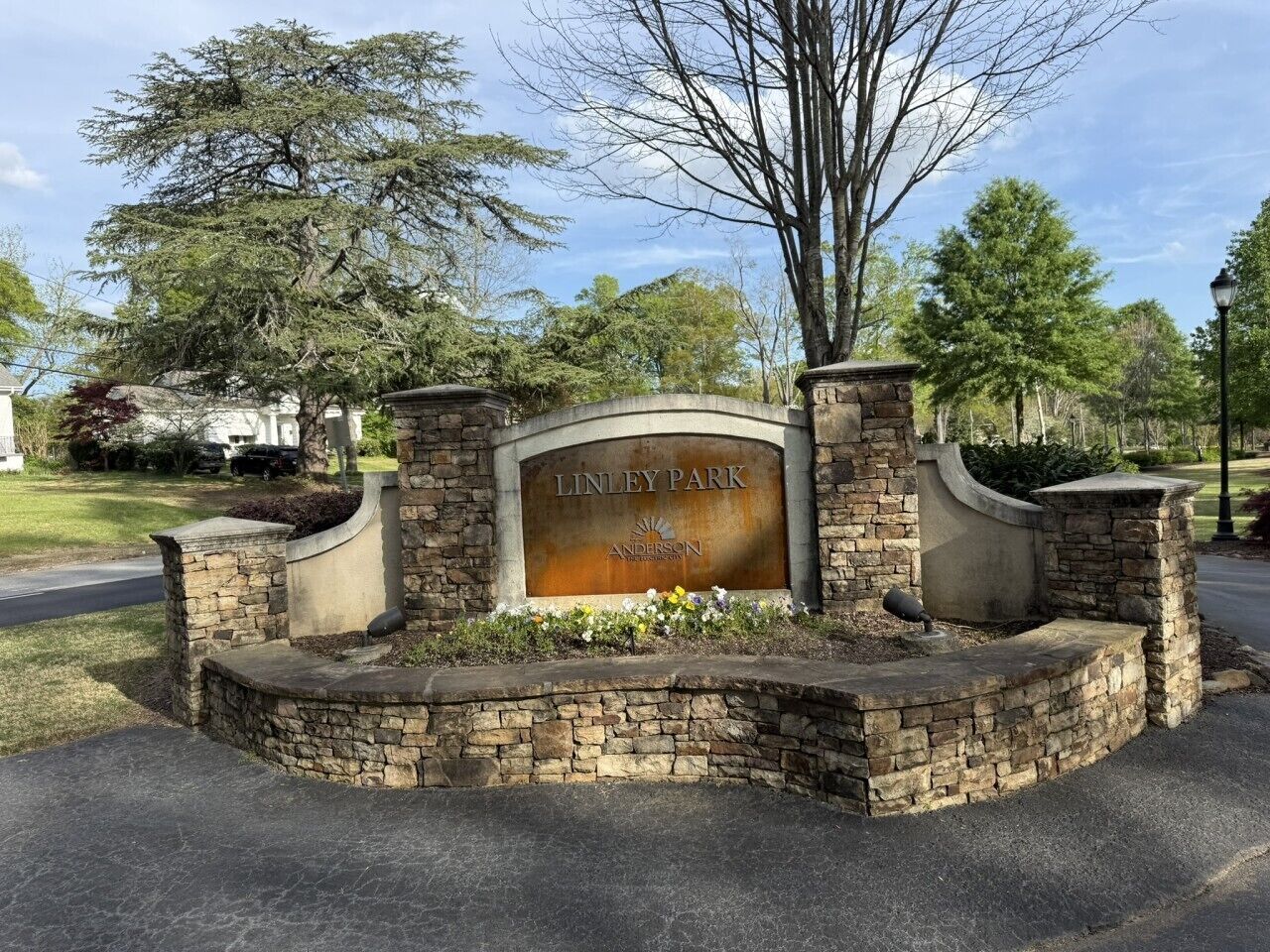 A stone entrance with a sign reading 'LINLEY PARK ANDERSON' surrounded by a landscaped area with flowers.