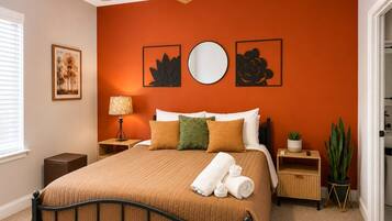A bedroom with a bed, a nightstand, a lamp, a potted plant, and artwork on the wall.