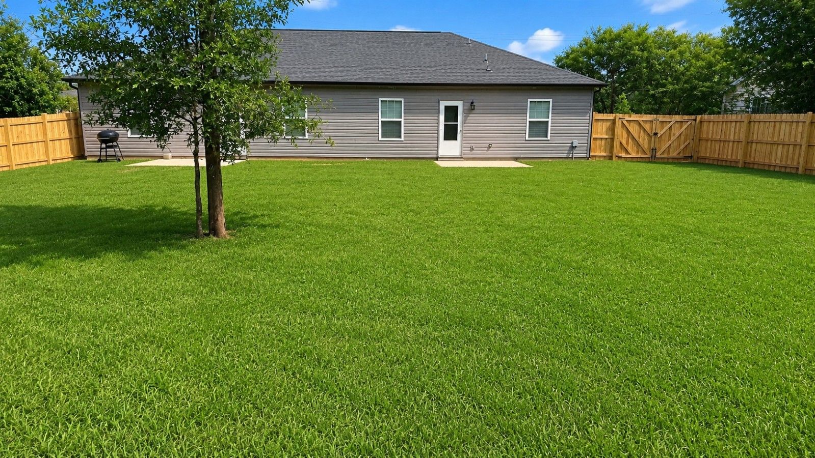 A residential property with a well-maintained lawn, a wooden fence, and a house with a gray exterior.