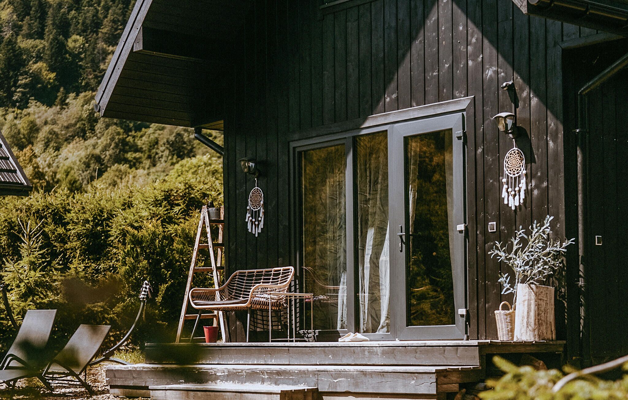 A wooden cabin with a sliding glass door, a chair, a ladder, and a basket on the porch.