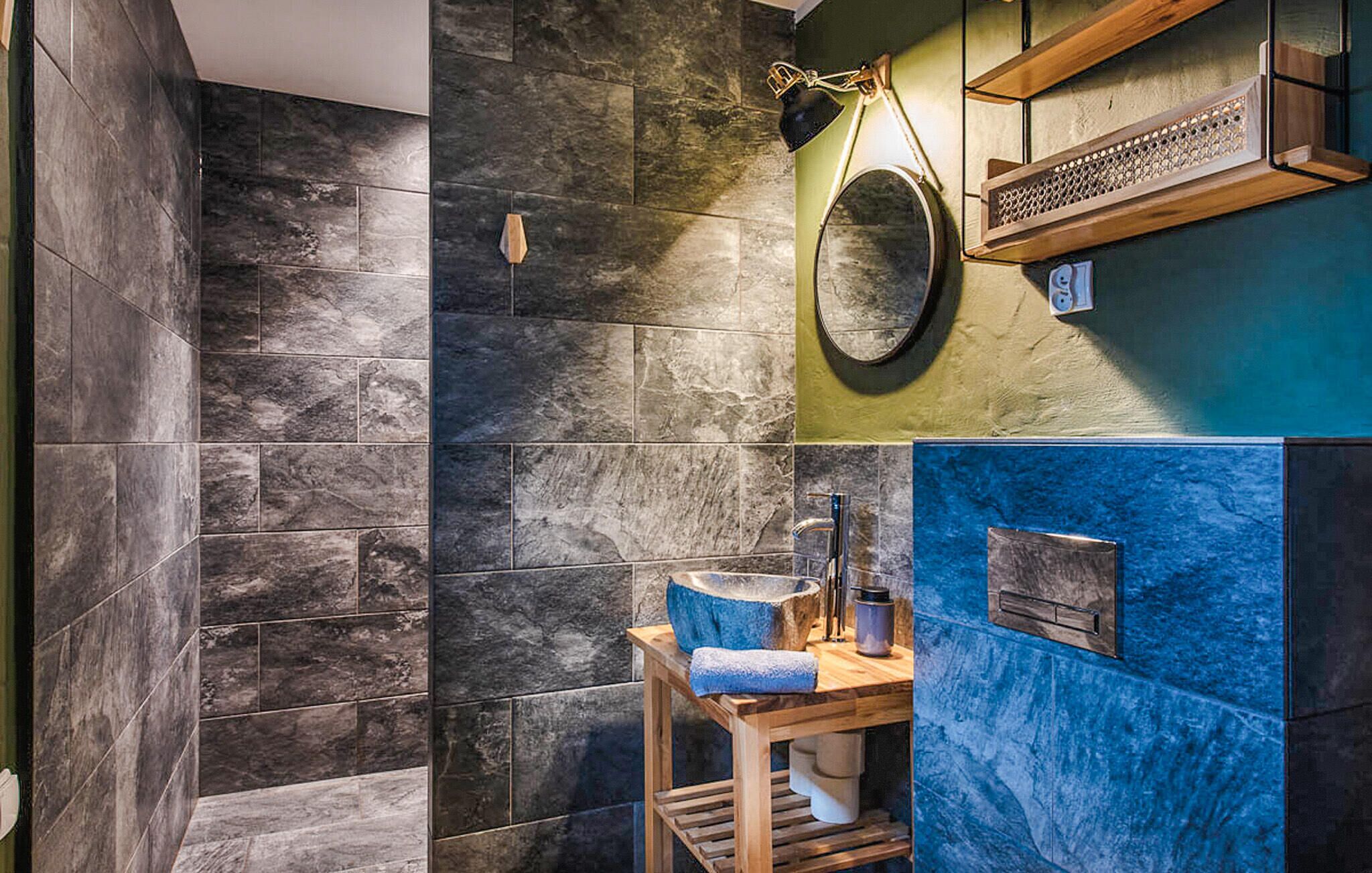 A bathroom with dark stone tiles, a wooden vanity with a sink, and a mirror.
