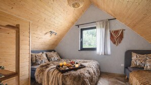 Une chambre mansardée chaleureuse avec un plafond en pente, une fenêtre avec des rideaux, un lit recouvert d’un plaid en fausse fourrure et un plateau contenant des éléments pour le petit-déjeuner.