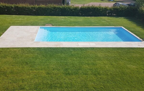 Ein rechteckiger Swimmingpool mit glasklar blauem Wasser, umgeben von einer gepflegten Rasenfläche und einem Heckenstreifen im Hintergrund.