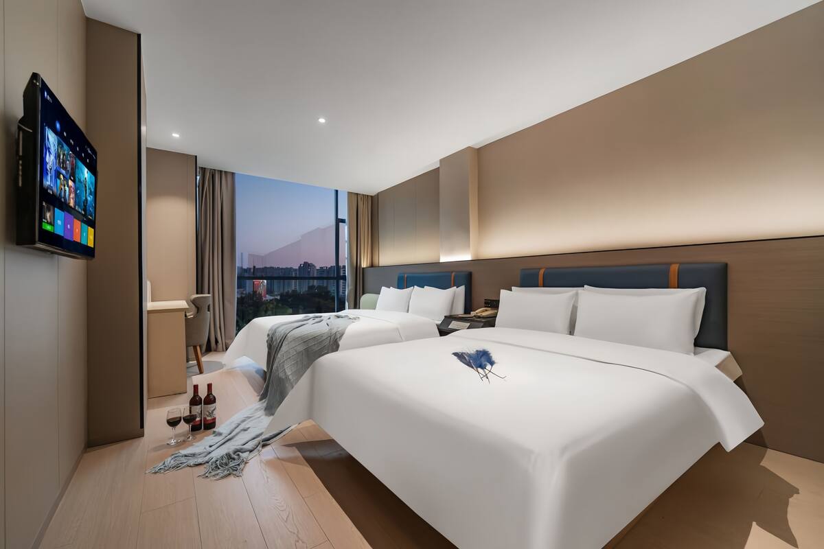 A modern hotel room with two beds, a TV, and a city view.