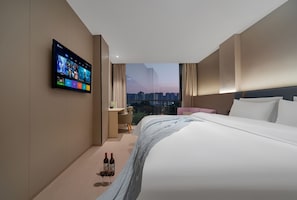 A modern hotel room with a large bed, a flat-screen TV mounted on the wall, a city view through the window, and a small seating area. - Buffle Hotel Shenzhen Xixiang Bihaiwan (Shenzhen)