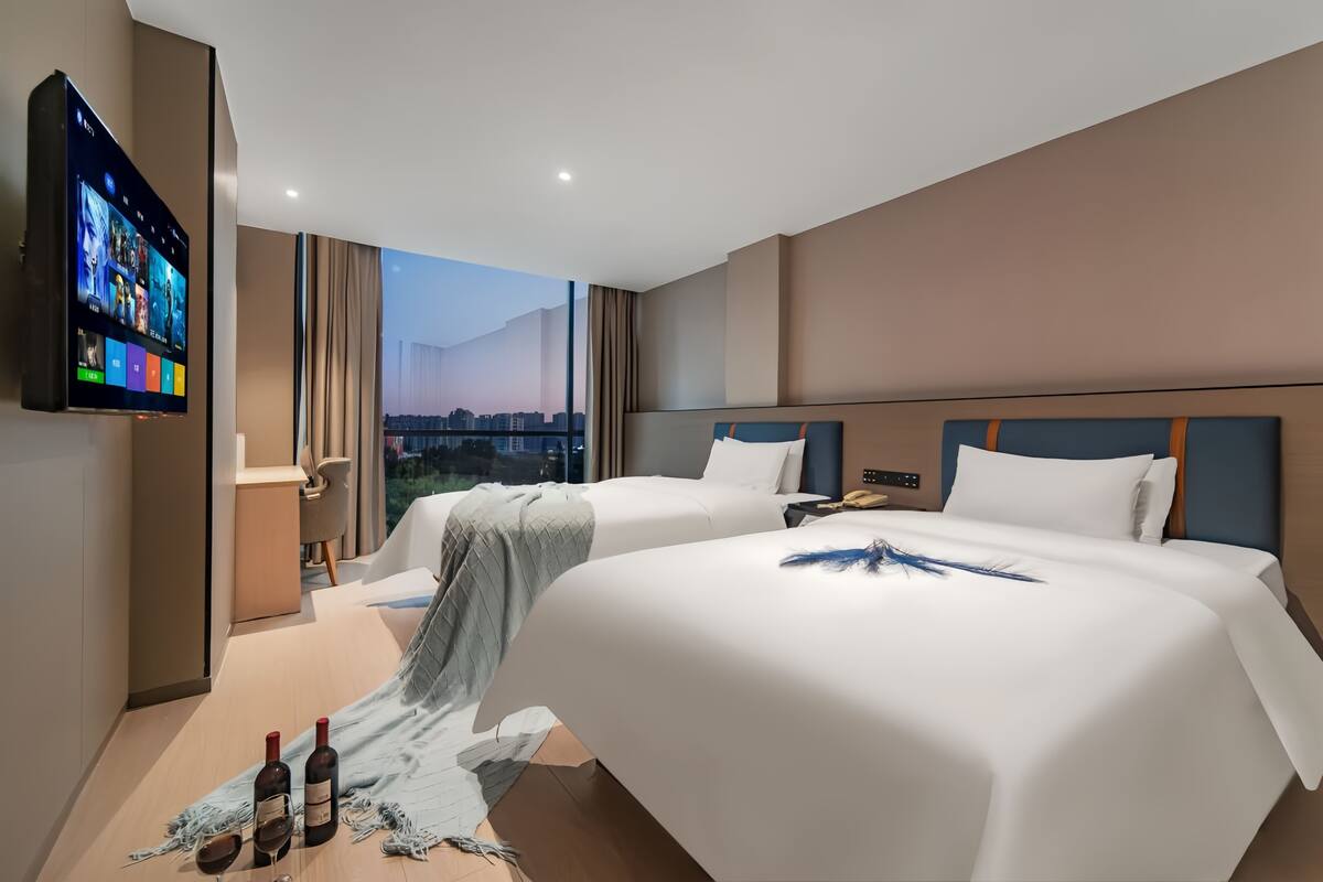 A hotel room with two beds, a TV, and a city view.