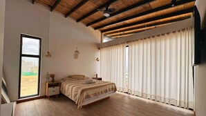 Un dormitorio con una cama grande, suelo de madera, ventilador de techo y vistas por una ventana.
