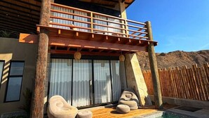 Un edificio moderno con balcón de madera, ventanas amplias y un área de piscina con sillones de descanso.
