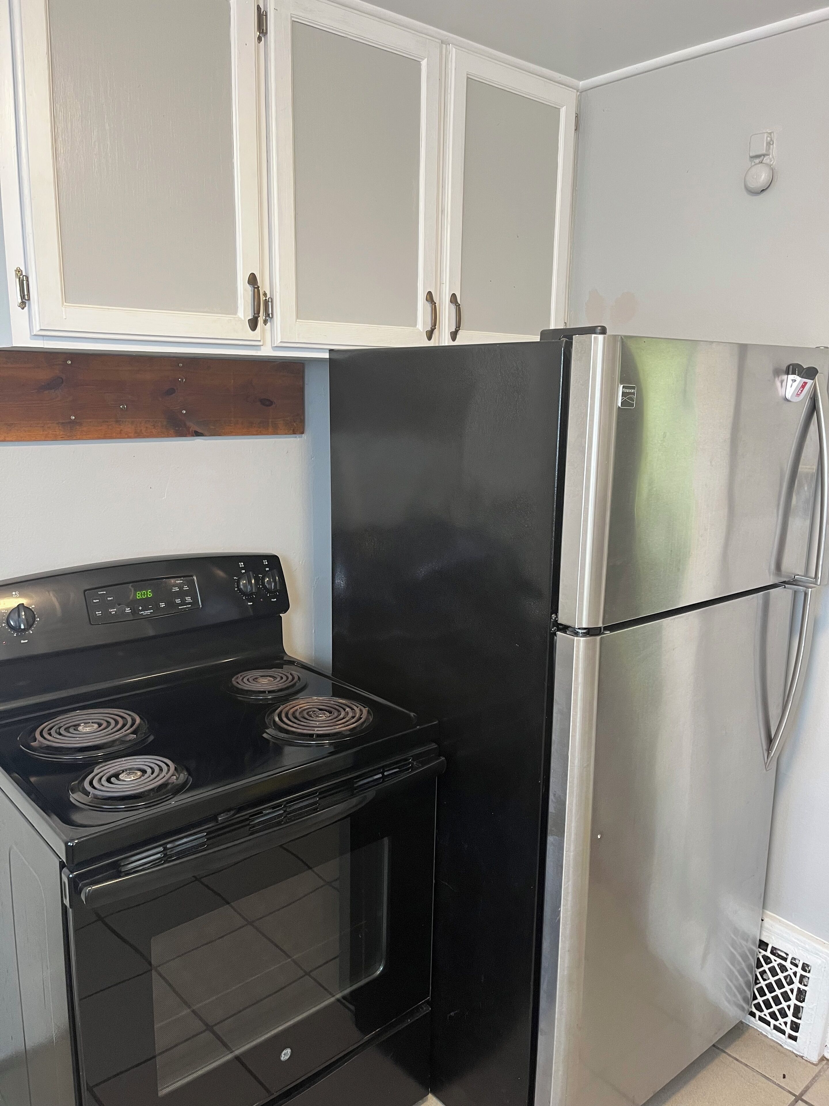 A kitchen with a black stove, stainless steel refrigerator, and white cabinets.