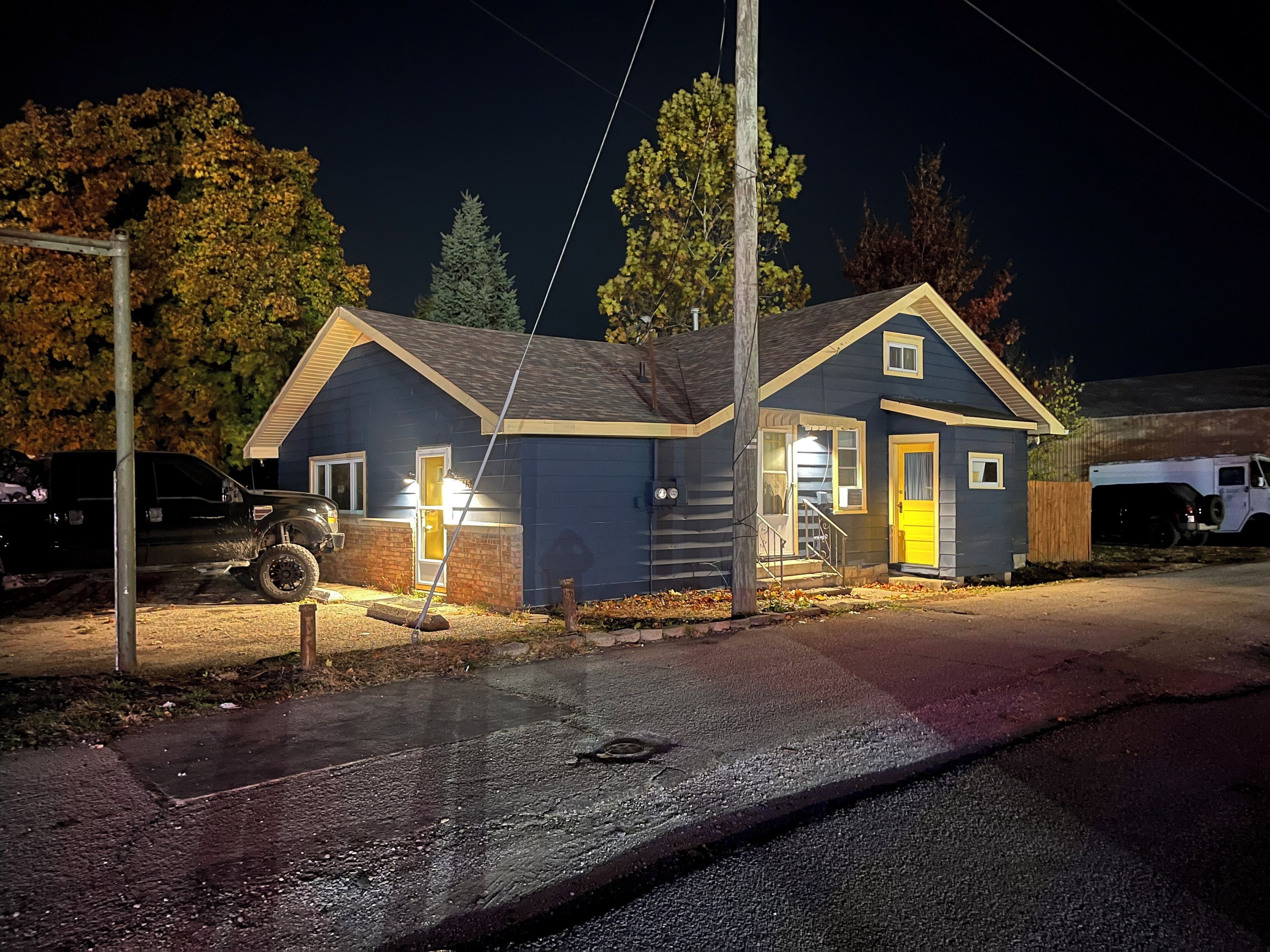 Una piccola casa a un piano con portico anteriore e garage, illuminata da luci esterne di notte.