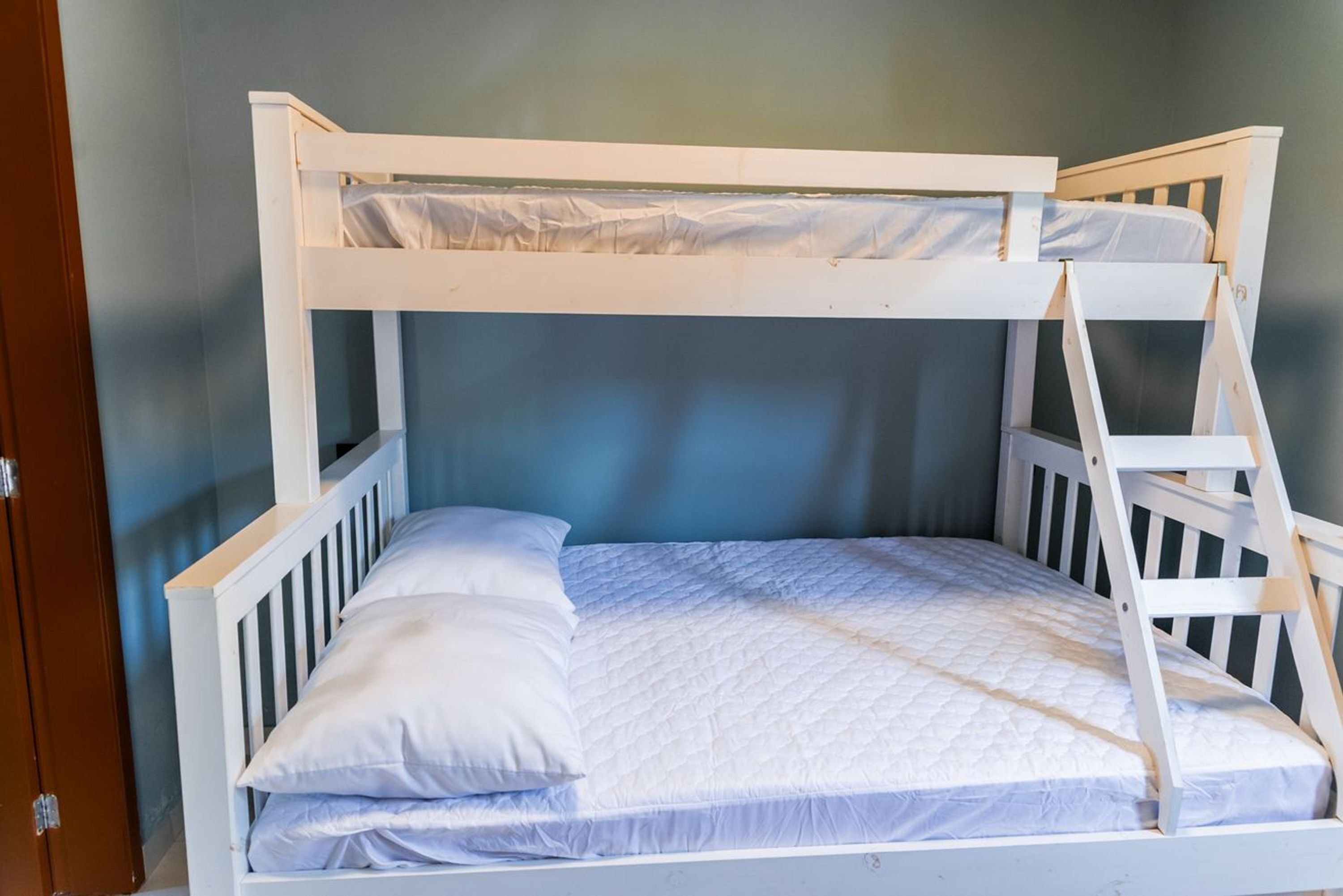 Una cama litera con escalera, ropa de cama blanca y una puerta a la izquierda.