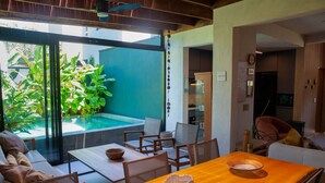 A modern dining area with a wooden table, chairs, and a view of a swimming pool and lush greenery. - Casa Premium com Piscina e rea Gourmet - Camburi (São Sebastião)
