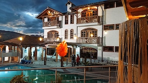Ein zweistöckiges Gebäude mit Swimmingpool, hölzernen Balkonen und einer großen orangefarbenen Blüte im Vordergrund.