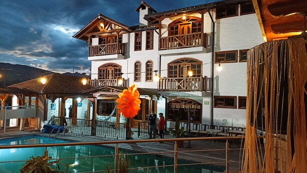 Un bâtiment à deux étages doté d’une piscine, de balcons en bois et d’une grande fleur orange au premier plan.