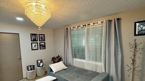 Une chambre à coucher moderne avec un canapé-lit gris, un lustre, des tableaux encadrés accrochés au mur et un porte-manteau.