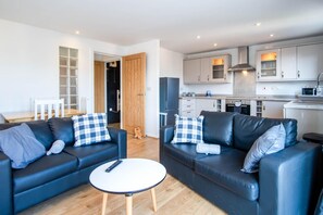 A modern living room with two black leather sofas, a round white coffee table, and a wooden dining table with chairs. - Ocean View - 2 Bedroom Apt - Llanelli (Llanelli)