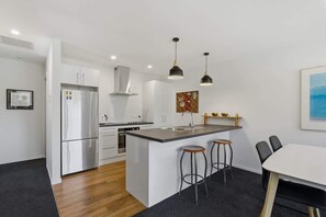 A modern kitchen with a central island, bar stools, and pendant lighting. - Northlake Nook (Wānaka)