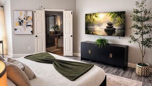 A bedroom with a bed, a TV, a plant, and a painting. - FIFA2026, Pool + FREE Heated Spa, ATTstadium, Six Flag (Grand Prairie)